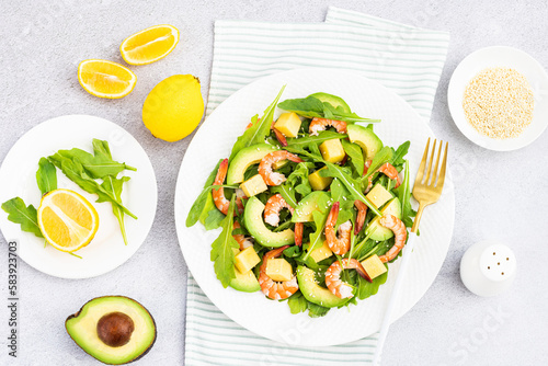 Flat lay of Healthy salad plate. Fresh seafood recipe. Grilled shrimps and fresh vegetables (avocado, arugula, mango) on gray concrete background. 