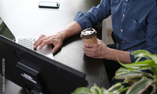 Mans hand with coffee cap at the desk with laptop in office.
