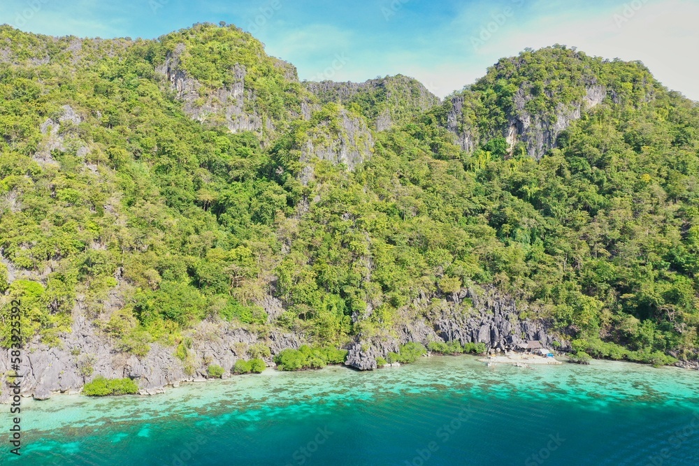 Panorama drone shot of majestic rocks in Coron, Palawan in the Philippines, covered with bushes and surrounded by the sea.