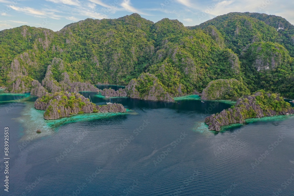Panorama drone shot of majestic rocks in Coron, Palawan in the Philippines, covered with bushes and surrounded by the sea.