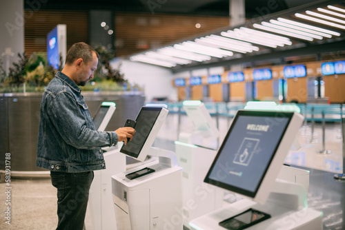 A male passenger at the electronic check-in desk in the departure area of the modern airport terminal.