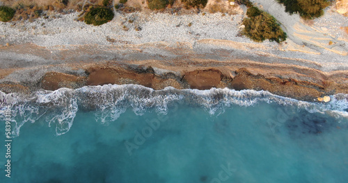 Canvastavla Flying drone over the coastline of the island overlooking rocky shoreline with vegetation and rocks and clear sea with light foamy waves in Cyprus