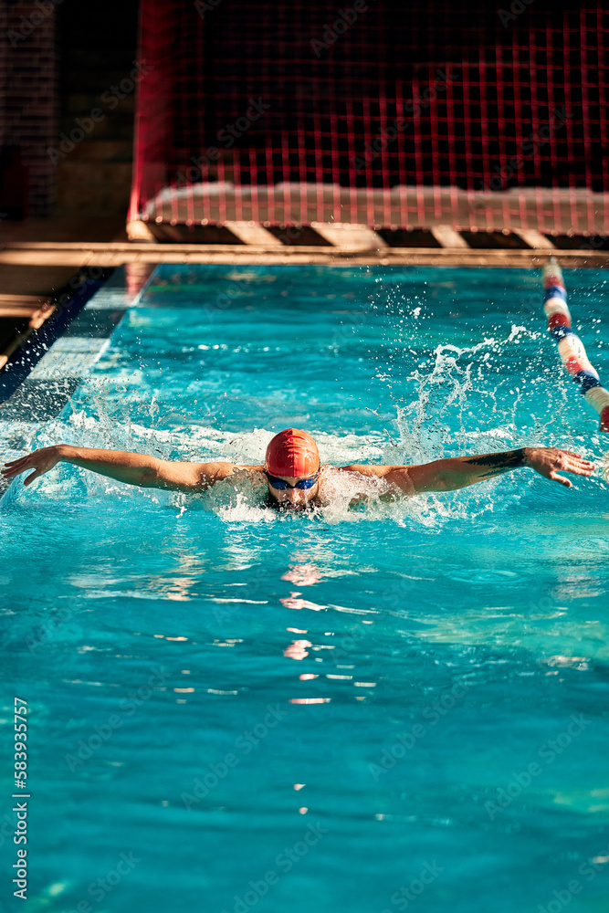 A man with a red cap swims in a blue pool, head-on shot