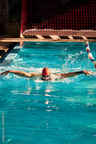 A man with a red cap swims in a blue pool, head-on shot