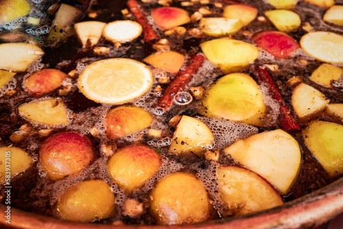 Closeup shot of traditional mulled wine with cinnamon sticks, oranges, and apples. © Pez Photography/Wirestock Creators