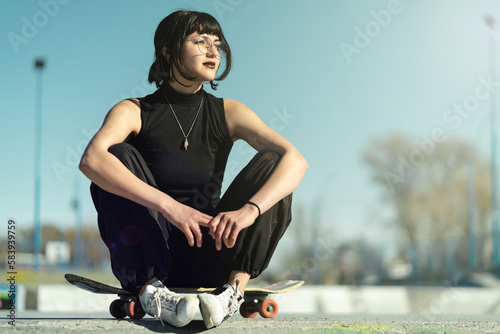 Принти на полотні Pretty young girl wearing glasses sitting on her skateboard in the floor towards