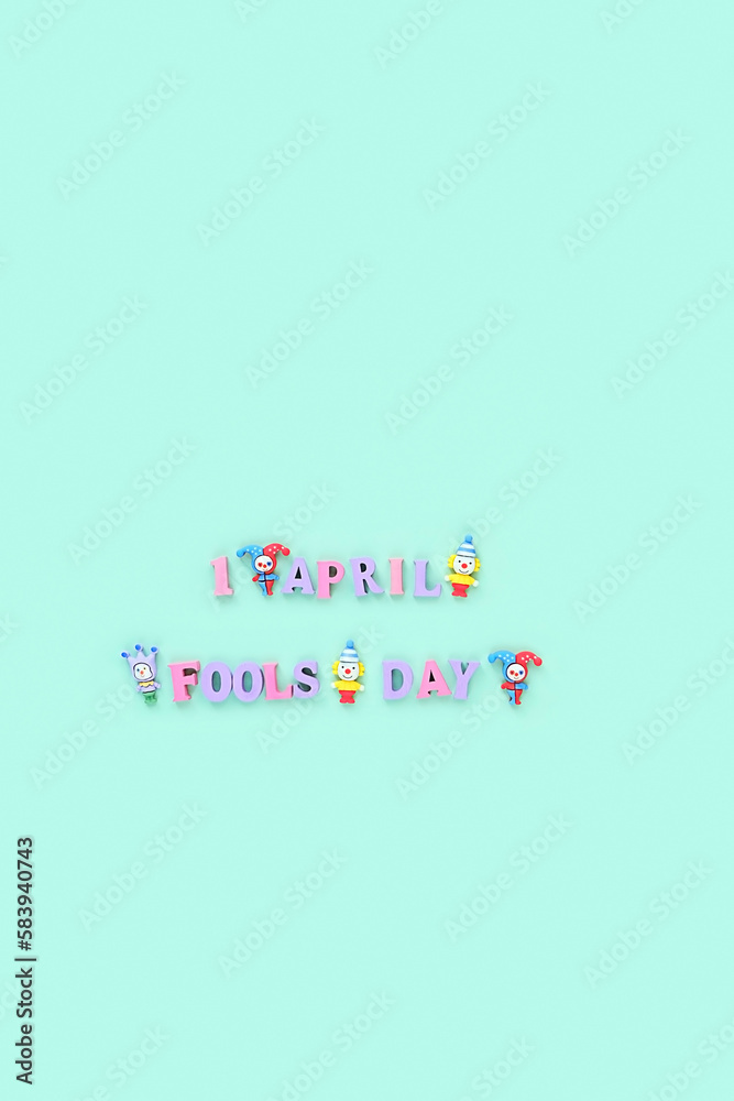 Fototapeta premium 1 april date, Fool's day text made of wooden letters, decorative miniature clowns on abstract green background. Greeting festive card. minimal creative design. flat lay