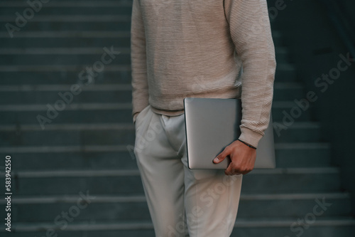 Close up view of man that is standing against the stairs outdoors and holding laptop