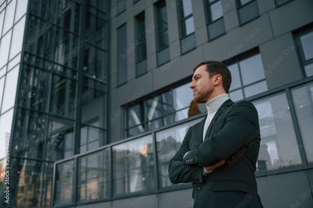 Standing with arms crossed. Handsome man in formal clothes is outdoor near the business building Standing with arms crossed. Handsome man in formal clothes is outdoor near the business building