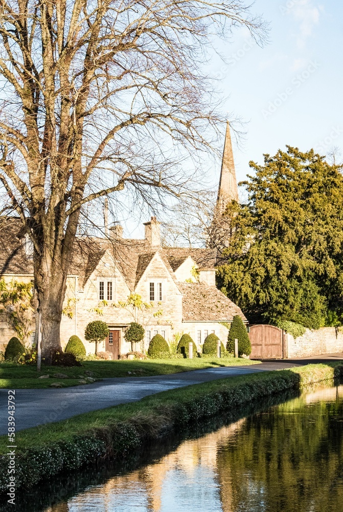 Fototapeta premium Row of historic quintessential Cotswold cottages by a river in Cotswolds, England, vertical shot
