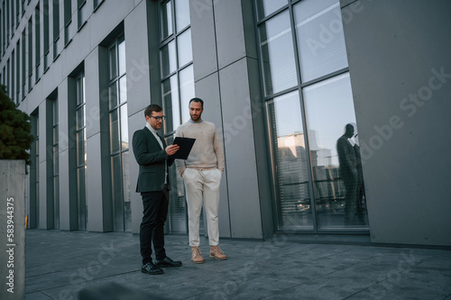 With notepat and documents. Businessman in formal clothes is with black man outdoors in the city
