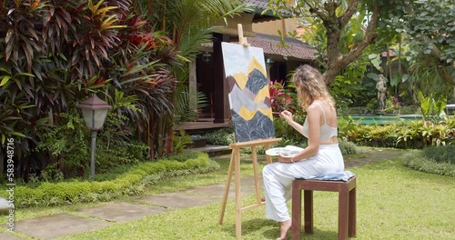 Creative young female artist painting a picture with acrylic paints outdoors. Creativity, hobby and art concept