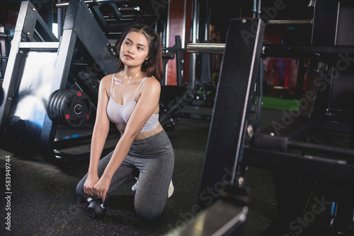 A young asian woman admires her sexy physique on the mirror after a set of goblet squats with a kettlebell. Training at a modern gym.