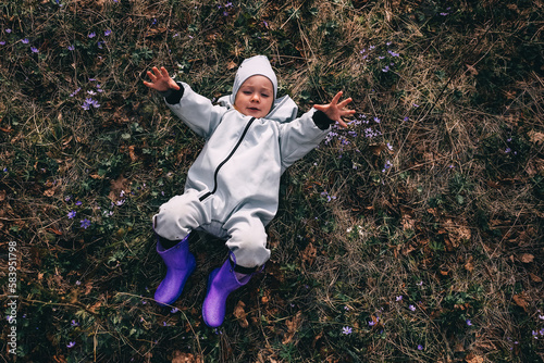 Little girl in violet boots and blue overall lying in spring blooming forest photo
