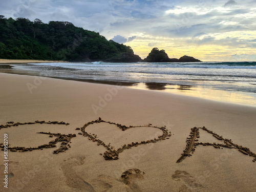 Fototapeta Naklejka Na Ścianę i Meble -   Love demonstration on the prettiest beach in the world with a gorgeous sunset in the background. Picture taken in Sancho beach located in the archipelago Fernando de Noronha, Brazil. .
