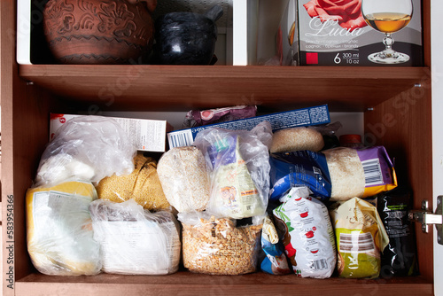 Unorganized storage of cereals in the kitchen cabinet. Macaroni, sugar, buckwheat, corn balls in sack bags.