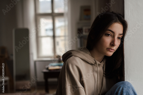 Photography Unhappy teenage girl sitting in home and looking out of window.