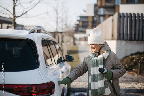 Close up of senior woman charging electric car.