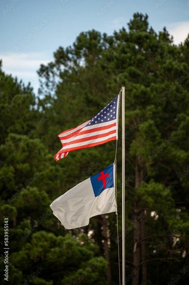 Vertical shot of an American and Christian flag on a pole in a park