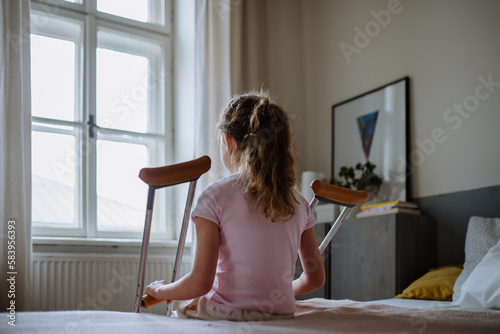 Rear view of little girl with broken leg sitting on a bed.
