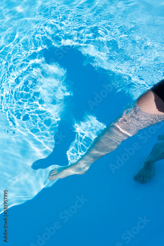 une jambe et une silhouette en ombre sur l'eau de la piscine