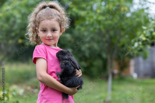 little cute girl playing with little black rabbit. Child with pet bunny outdoors. Happy kid with animal. Happy Easter concept