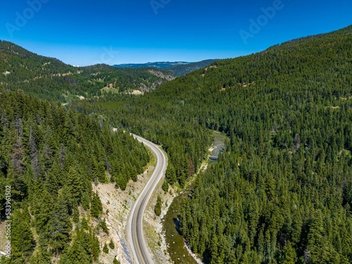 Drone view of Crowsnest Highway by river passing through rocks  dense forests and mountains  Canada.