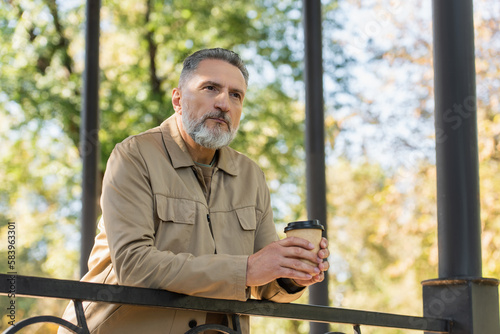 Middle aged man holding coffee to go on bridge in spring park. © LIGHTFIELD STUDIOS
