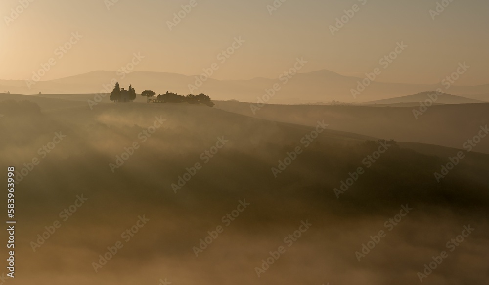 Beautiful landscape of Val d'Orcia at sunset with a yellow sky in the background, Tuscany, Italy
