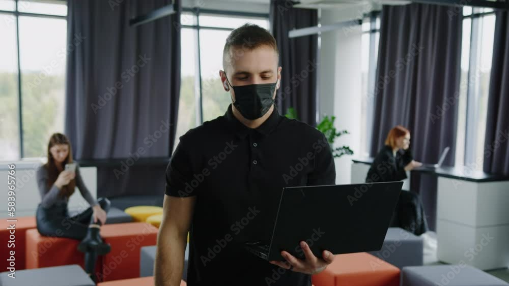 Office work during the flu pandemic. Portrait of a man with a laptop in the office. Colleagues in the background in an open space Office work during the flu pandemic. Portrait of a man with a laptop in the office. Colleagues in the background in an open space
