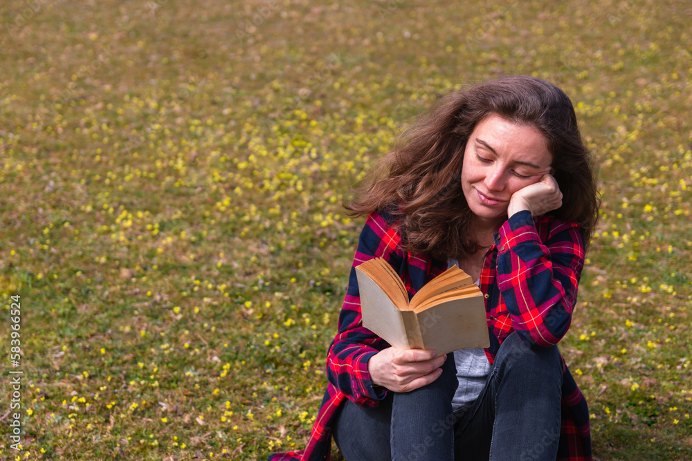 Portrait of a happy young woman reading a book and sitting on the grass Portrait of a happy young woman reading a book and sitting on the grass