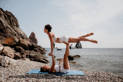 Woman sea yoga. Two Happy women meditating in yoga pose on the beach, ocean and rock mountains. Motivation and inspirational fit and exercising. Healthy lifestyle outdoors in nature, fitness concept.