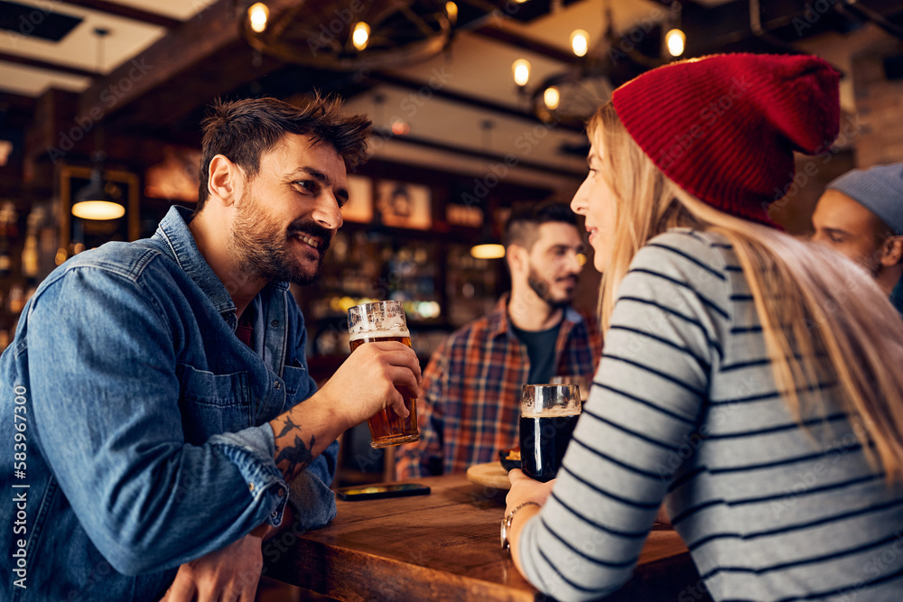 Happy man drinking beer and talking to female friend in pub.