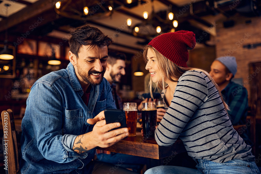Young happy couple using cell phone while having drink in bar.