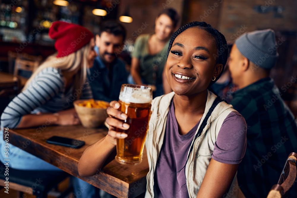 Happy black woman drinking beer with friends in pub and looking at camera.