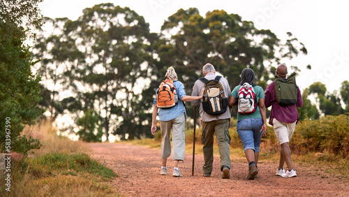 Rear View Of Active Senior Friends Enjoying Hiking Through Countryside Walking Along Track Together