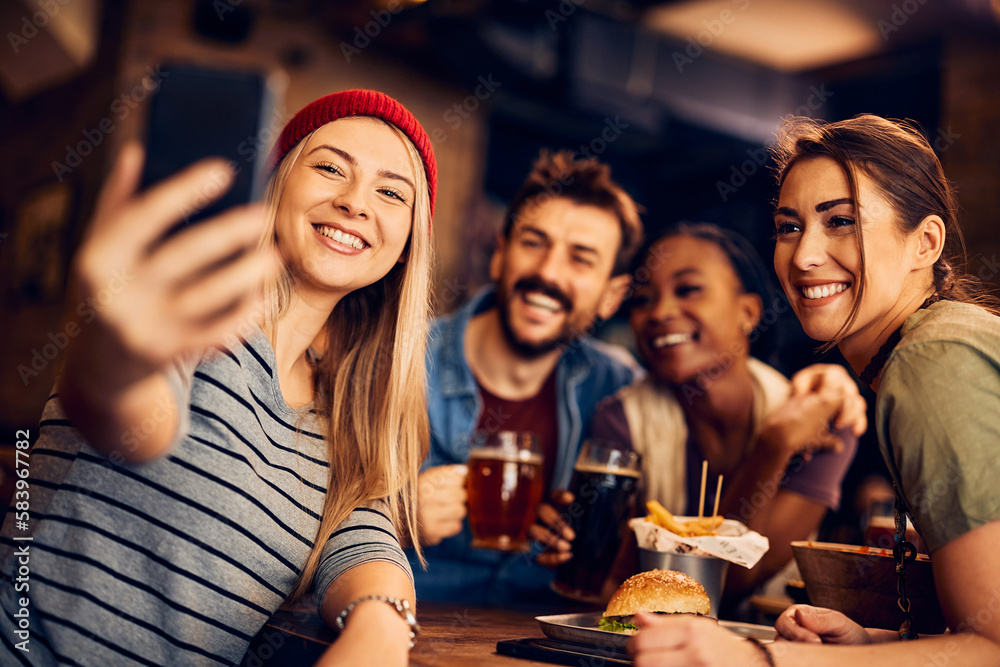 Young happy friends taking selfie with cell phone in bar.