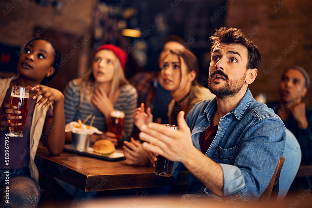 Young man and his friends watch sports game with anticipation in bar.