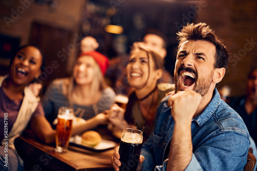 Sports fan screams while watching match on TV with his friends in pub.