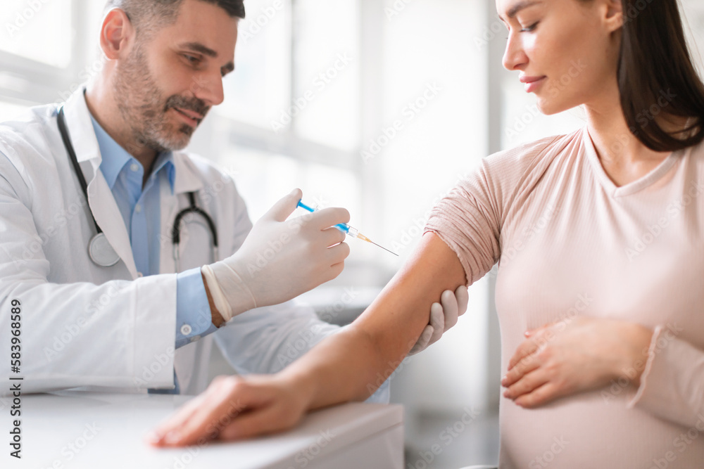 Fototapeta premium Vaccination in pregnancy. Pregnant woman getting vaccinated, male doctor giving vaccine shot injecting lady in arm