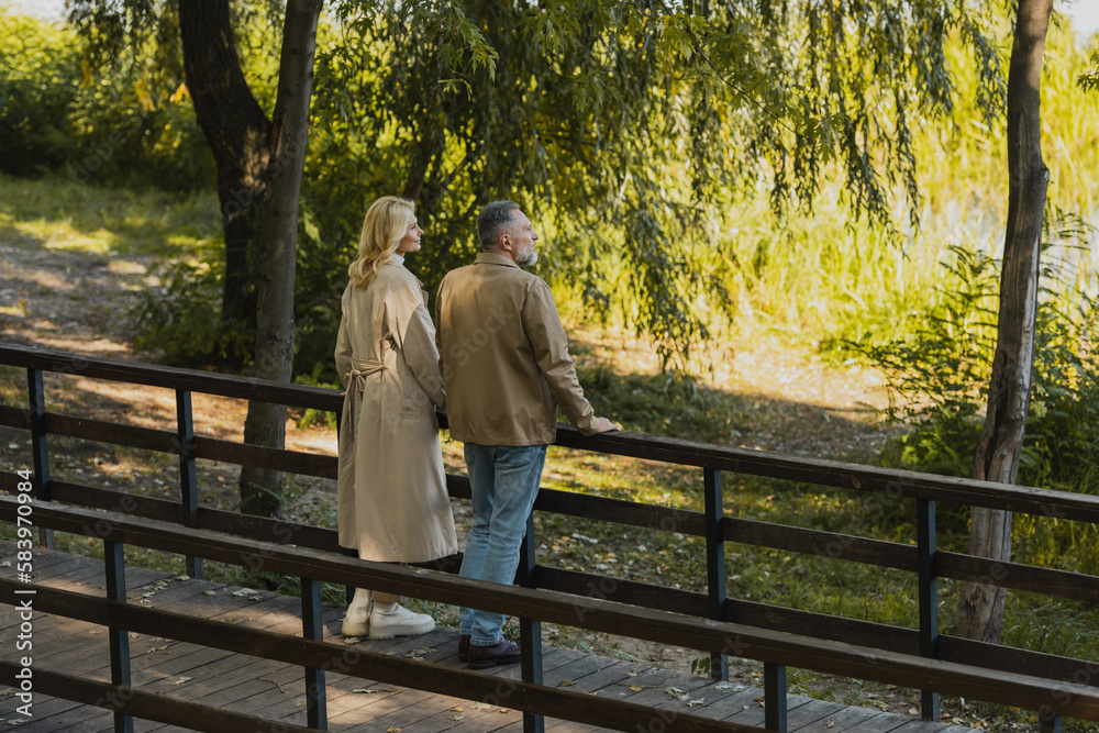 Fototapeta premium Side view of middle aged couple looking away while standing on bridge in spring park.