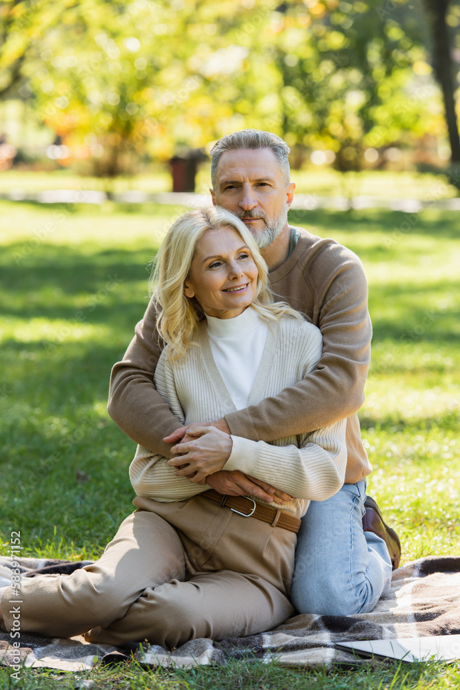 middle aged man with grey beard hugging charming blonde wife in green park. middle aged man with grey beard hugging charming blonde wife in green park.