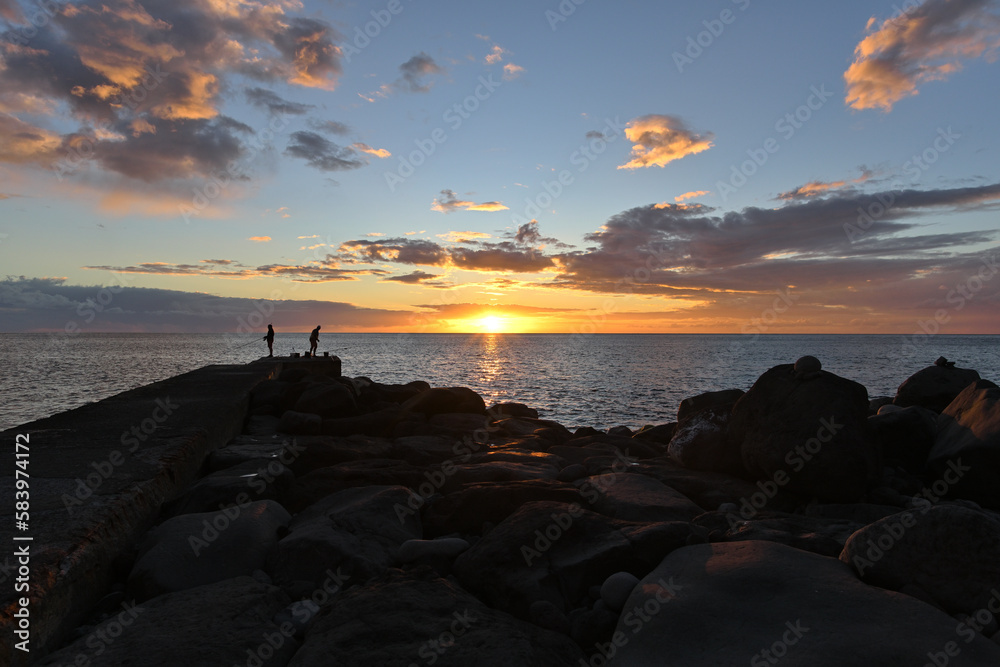 Ein schöner Sonnenuntergang über dem Meer und Angler stehen am Strand und Fischen