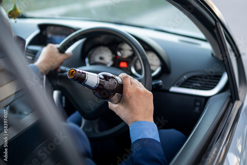 man in an expensive suit drinks beer at the wheel of a car causing the danger of an emergency. A businessman drinks while driving. Drunk driver concept