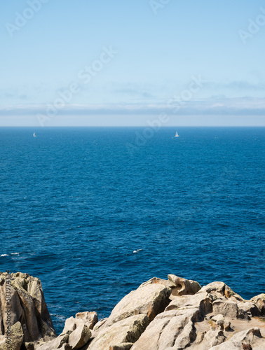 two sailboats in the ocean across a cliff