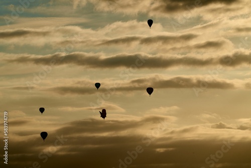Silhouette view of the hot air balloons flying high in cloudy dusk sky