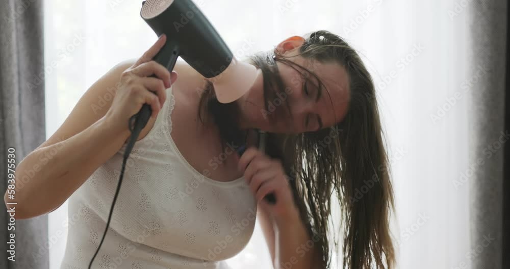 Beautiful young woman using hair dryer near the window at home Beautiful young woman using hair dryer near the window at home