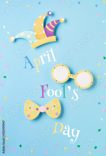 April Fool's Day holiday card with Jester hat, confetti and funny glasses on blue background, top view.