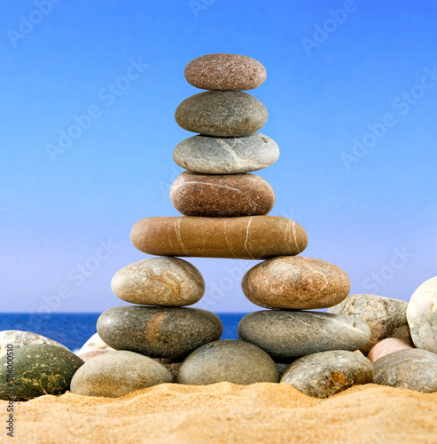 zen pyramid of stones on the sand against the background of the sea and blue sky