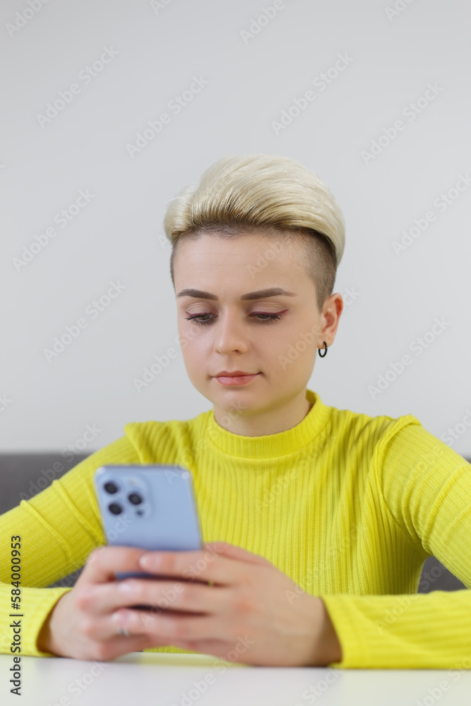 Beautiful tom boy female typing a message on modern smart phone. Stylish white female person with short hair using blue mobile phone Beautiful tom boy female typing a message on modern smart phone. Stylish white female person with short hair using blue mobile phone